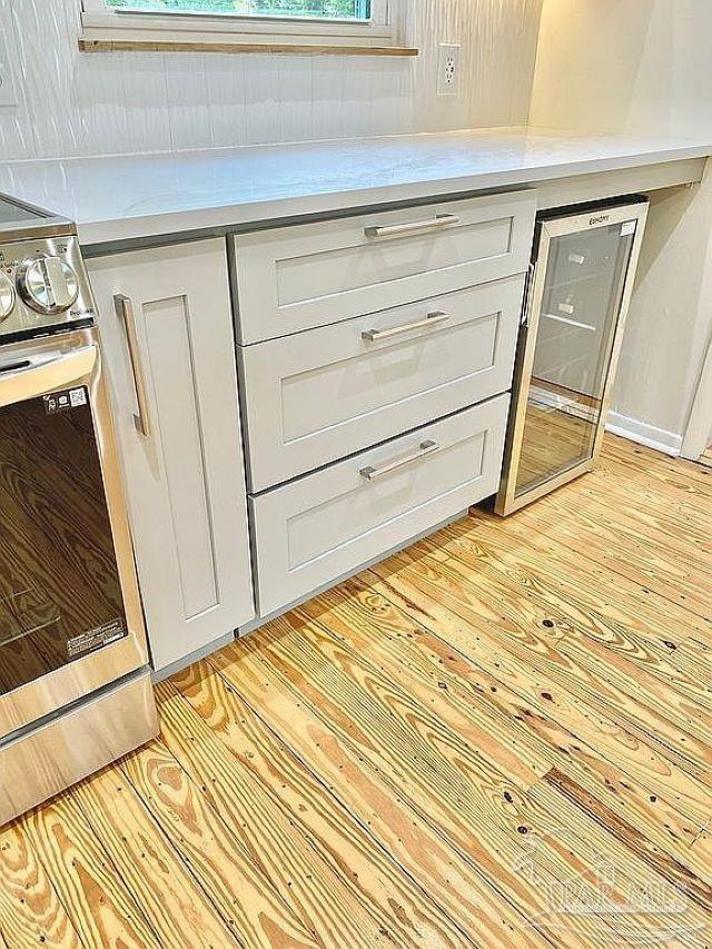 room details featuring light hardwood / wood-style flooring, beverage cooler, white cabinetry, and stainless steel range oven