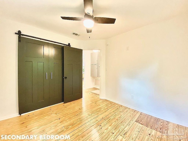 unfurnished bedroom featuring light hardwood / wood-style flooring, a closet, ceiling fan, and a barn door