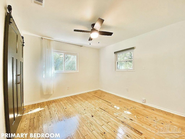 unfurnished room with ceiling fan, hardwood / wood-style flooring, a barn door, and a wealth of natural light