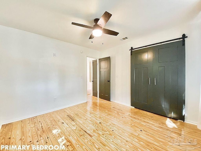 interior space featuring ceiling fan, light wood-type flooring, and a barn door