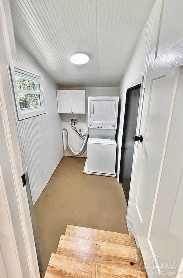 washroom featuring stacked washer and clothes dryer and cabinets