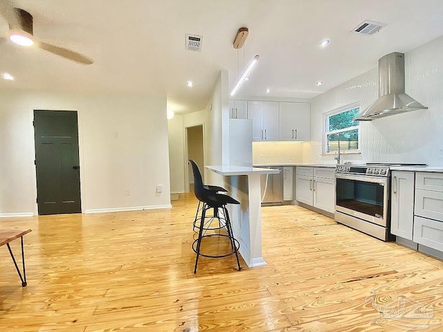 kitchen with light wood-type flooring, stainless steel appliances, wall chimney exhaust hood, and white cabinetry