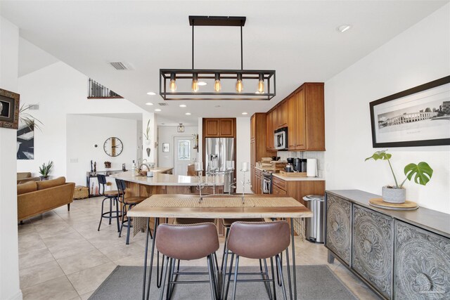 kitchen with a kitchen breakfast bar, brown cabinetry, stainless steel appliances, light countertops, and visible vents