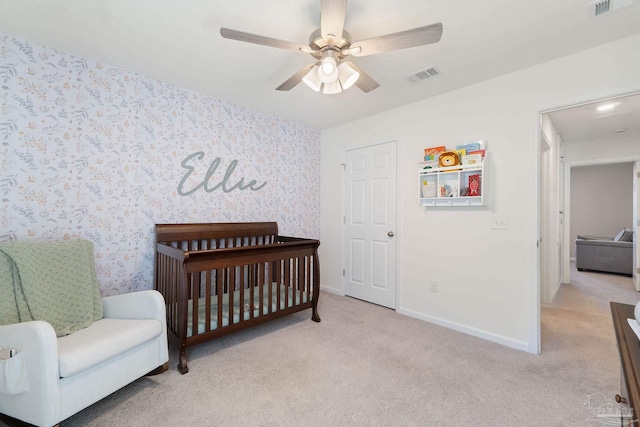 bedroom with a crib, wallpapered walls, baseboards, visible vents, and light colored carpet