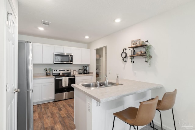 kitchen featuring stainless steel appliances, light countertops, white cabinetry, a sink, and a kitchen breakfast bar