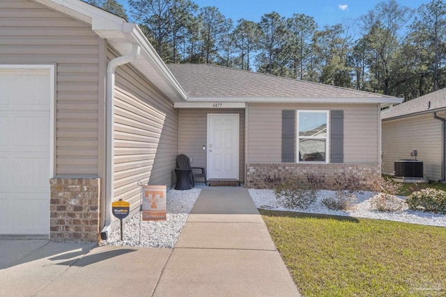 view of exterior entry with a garage, a shingled roof, and cooling unit