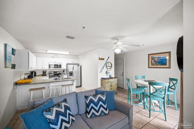 tiled living room featuring ceiling fan, sink, and a textured ceiling