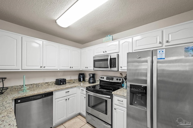 kitchen with light stone counters, white cabinets, stainless steel appliances, and light tile patterned floors