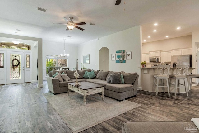 living room with ceiling fan with notable chandelier, crown molding, and dark wood-type flooring