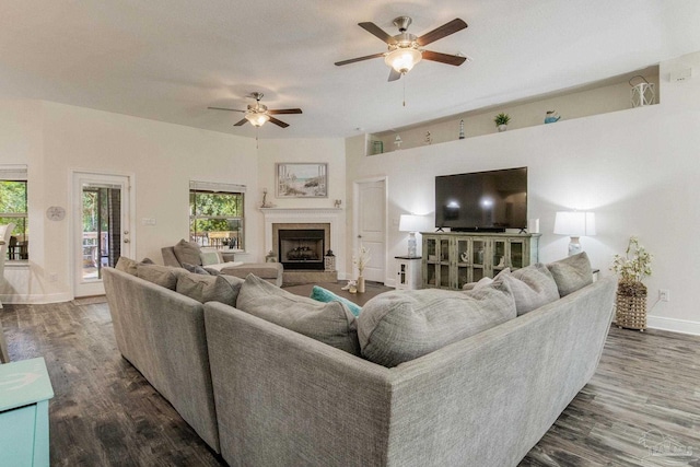 living room with a tile fireplace, ceiling fan, and dark wood-type flooring