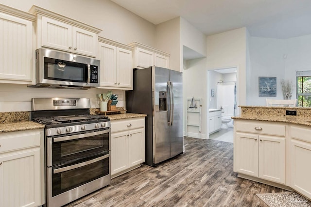 kitchen with light stone counters, cream cabinets, stainless steel appliances, and hardwood / wood-style flooring