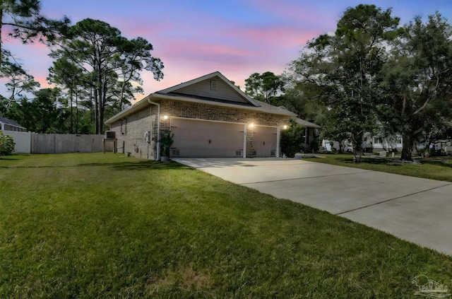 property exterior at dusk featuring a yard, concrete driveway, brick siding, and fence