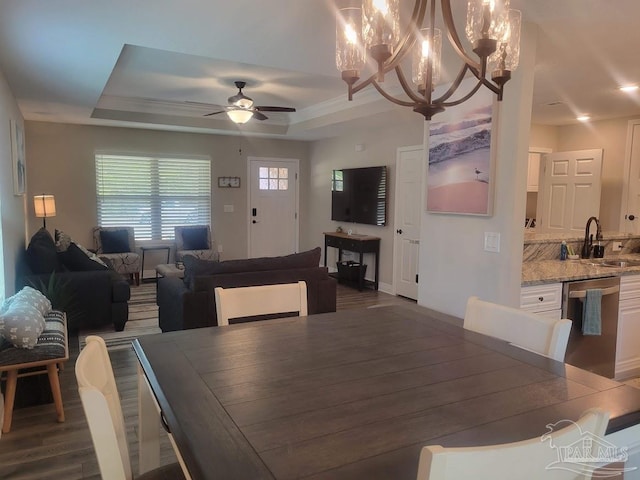 dining room with ceiling fan with notable chandelier, dark hardwood / wood-style flooring, sink, and a tray ceiling