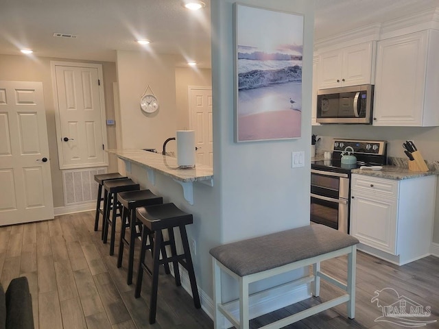 kitchen with white cabinets, hardwood / wood-style flooring, light stone countertops, and appliances with stainless steel finishes