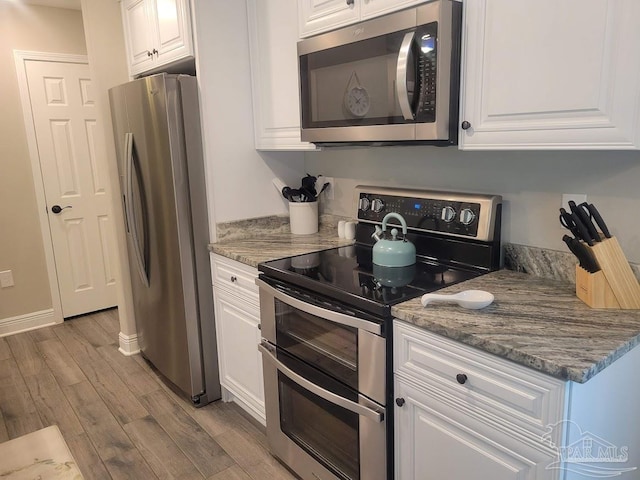 kitchen featuring dark stone countertops, white cabinetry, light hardwood / wood-style flooring, and appliances with stainless steel finishes