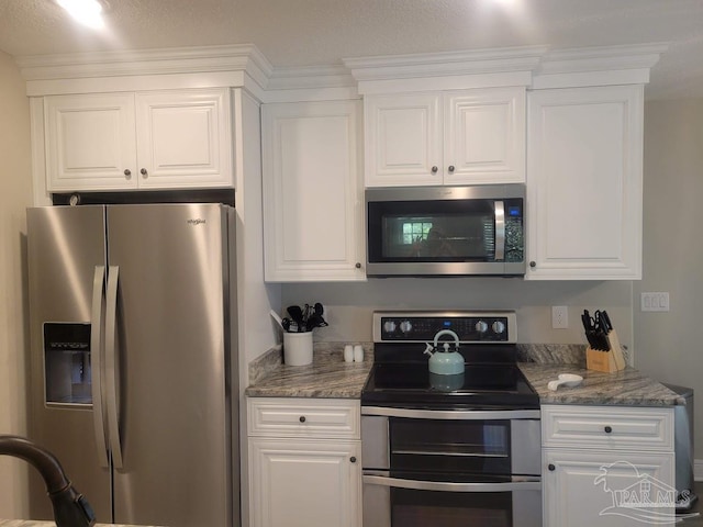 kitchen with white cabinetry, appliances with stainless steel finishes, and dark stone counters