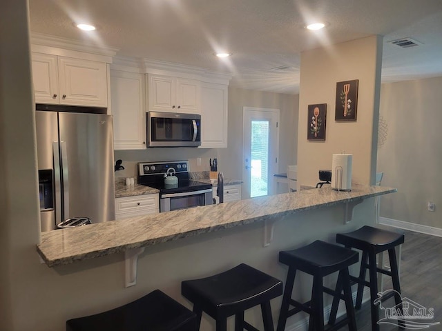 kitchen featuring dark hardwood / wood-style floors, white cabinetry, a breakfast bar area, and appliances with stainless steel finishes