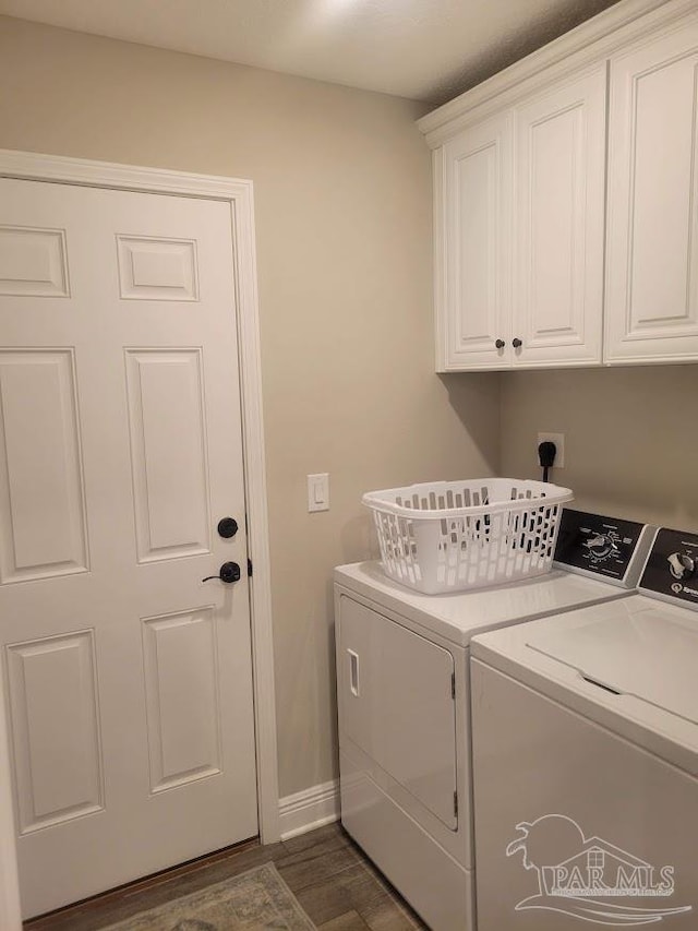 clothes washing area featuring washing machine and clothes dryer, dark wood-type flooring, and cabinets