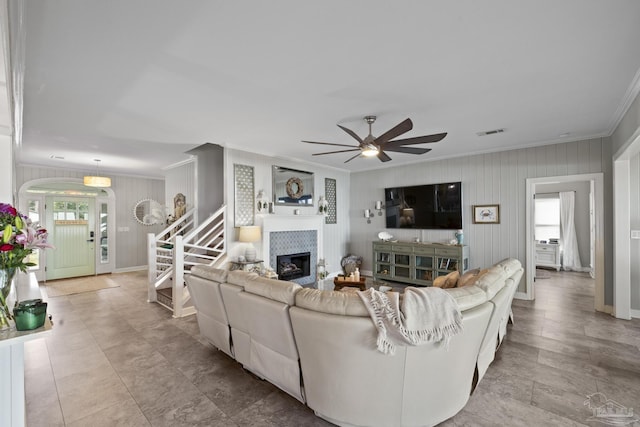 living room featuring a fireplace, visible vents, a ceiling fan, stairs, and ornamental molding