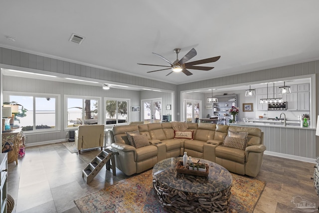 living area with ceiling fan, visible vents, and crown molding