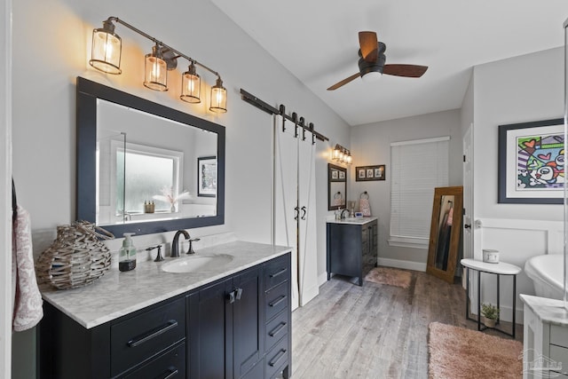 full bath featuring ceiling fan, wood finished floors, two vanities, a sink, and baseboards