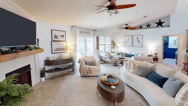 living area featuring lofted ceiling, ceiling fan, a textured ceiling, a fireplace, and visible vents