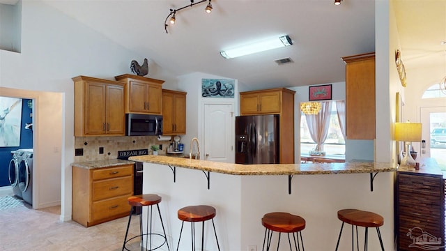 kitchen featuring visible vents, brown cabinets, a kitchen breakfast bar, independent washer and dryer, and refrigerator with ice dispenser