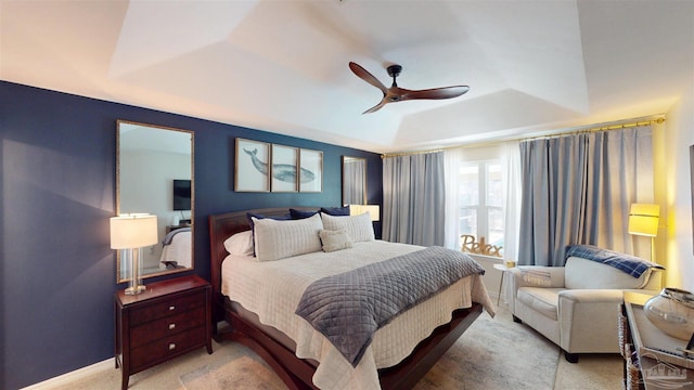 bedroom with a ceiling fan, a raised ceiling, light carpet, and baseboards