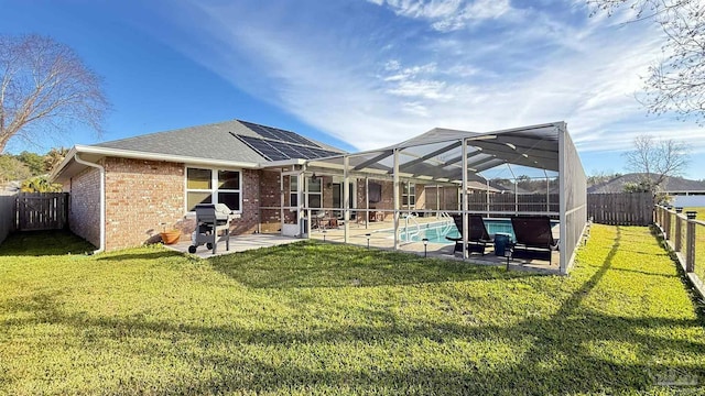 rear view of property featuring brick siding, a yard, a patio, solar panels, and a fenced backyard