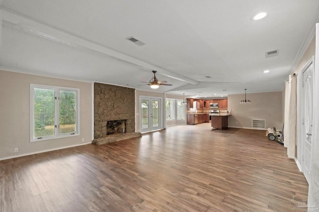 unfurnished living room with vaulted ceiling with beams, hardwood / wood-style flooring, a stone fireplace, crown molding, and ceiling fan