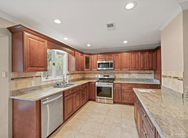 kitchen with sink, crown molding, light tile patterned floors, appliances with stainless steel finishes, and light stone counters