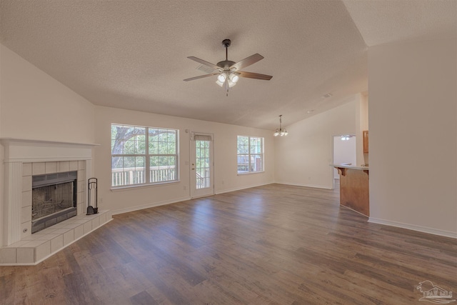 unfurnished living room with dark wood finished floors, a tiled fireplace, vaulted ceiling, a textured ceiling, and ceiling fan with notable chandelier