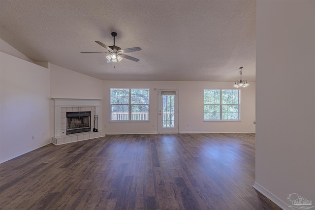 unfurnished living room featuring dark wood finished floors, a tiled fireplace, vaulted ceiling, a textured ceiling, and ceiling fan with notable chandelier