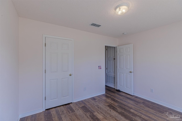 unfurnished bedroom featuring dark wood-style flooring, visible vents, a textured ceiling, and baseboards