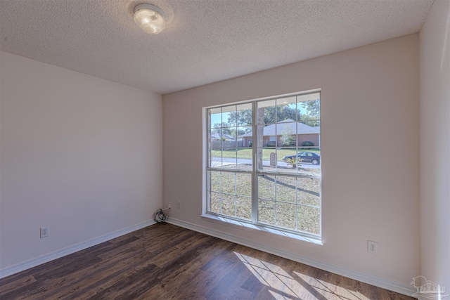 empty room featuring dark wood finished floors, a textured ceiling, and baseboards