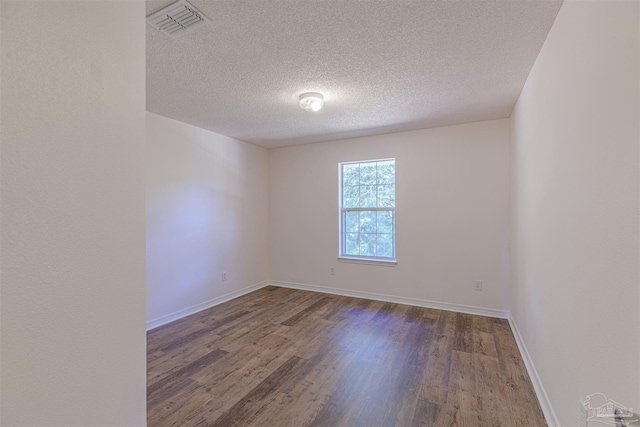 unfurnished room featuring a textured ceiling, wood finished floors, visible vents, and baseboards