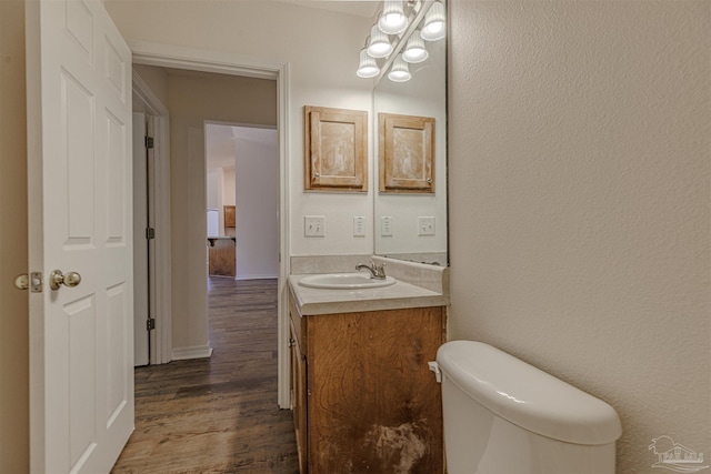 half bath featuring toilet, a textured wall, wood finished floors, and vanity