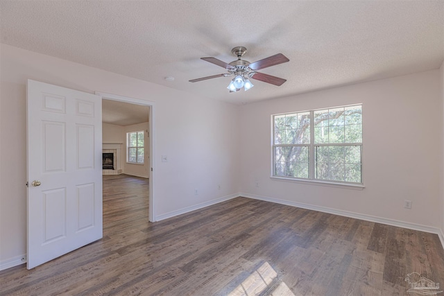 unfurnished room featuring dark wood finished floors, a tiled fireplace, ceiling fan, a textured ceiling, and baseboards