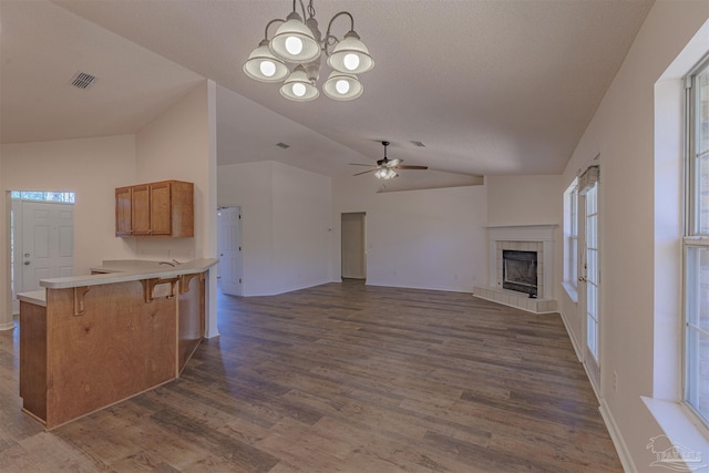 unfurnished living room featuring visible vents, dark wood-type flooring, vaulted ceiling, a tile fireplace, and ceiling fan with notable chandelier