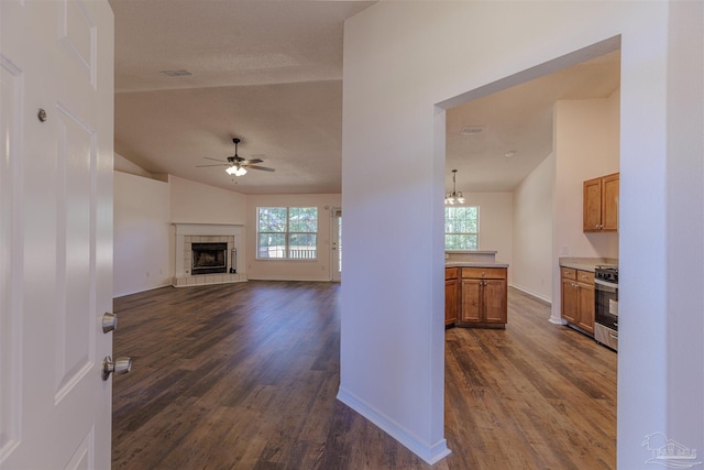 interior space with baseboards, dark wood finished floors, a tile fireplace, lofted ceiling, and ceiling fan with notable chandelier