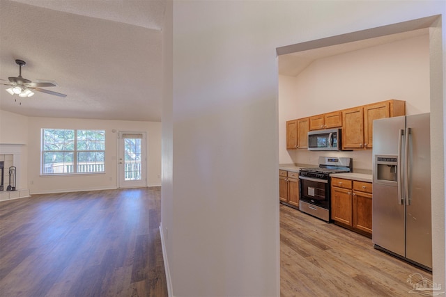 kitchen with brown cabinets, light countertops, light wood-style flooring, appliances with stainless steel finishes, and open floor plan