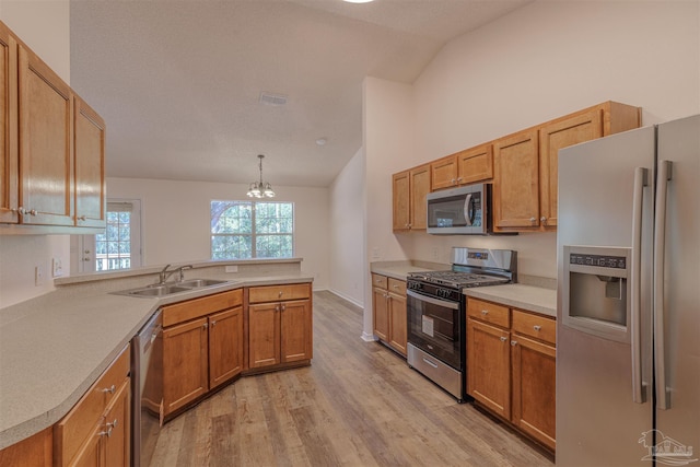 kitchen with lofted ceiling, a peninsula, a sink, light countertops, and appliances with stainless steel finishes