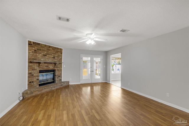 unfurnished living room featuring french doors, a brick fireplace, a textured ceiling, ceiling fan, and hardwood / wood-style flooring