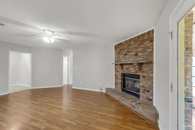 unfurnished living room featuring ceiling fan, wood-type flooring, a textured ceiling, and a brick fireplace