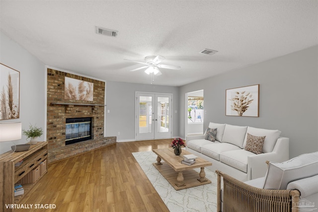 living room with a fireplace, a textured ceiling, light hardwood / wood-style floors, and ceiling fan