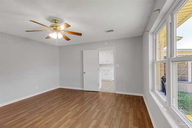 spare room with ceiling fan, light wood-type flooring, and a textured ceiling