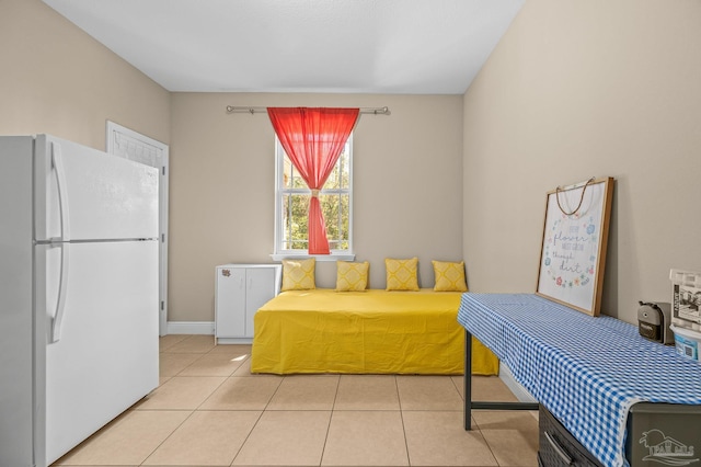 bedroom featuring freestanding refrigerator, light tile patterned floors, and baseboards