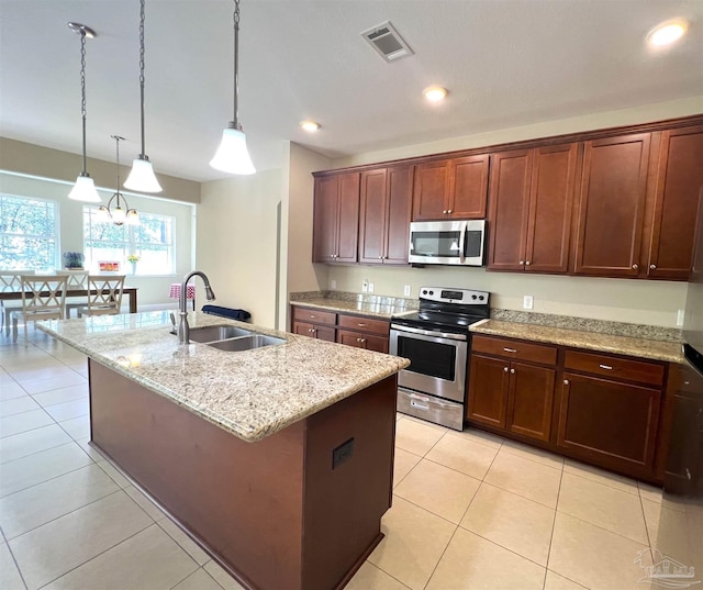 kitchen featuring appliances with stainless steel finishes, a sink, light stone countertops, a center island with sink, and decorative light fixtures
