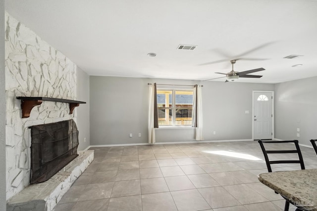 unfurnished living room with a stone fireplace, ceiling fan, and light tile patterned floors