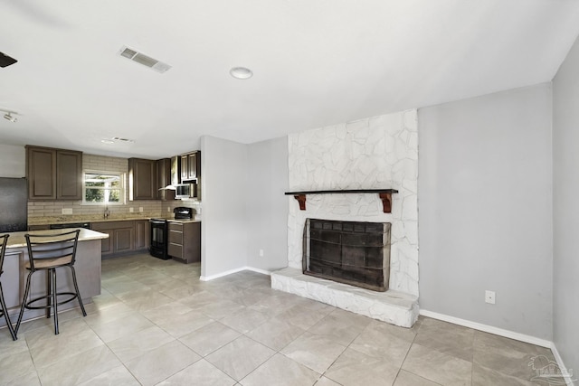 kitchen with black stove, dark brown cabinets, a fireplace, a breakfast bar area, and light tile patterned flooring